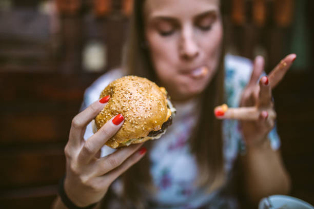 mujer disfrutando de la deliciosa hamburguesa - comer fotografías e imágenes de stock