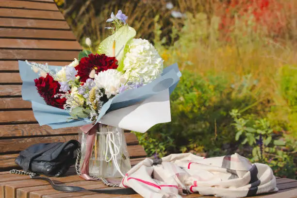 A bouquet of flowers on a bench in the autumn park as a concept of waiting for a romantic meeting.