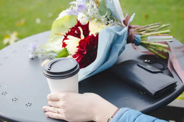 The girl at a table in an outdoor cafe. On the table, a bouquet of flowers as a symbol of romantic relationships.