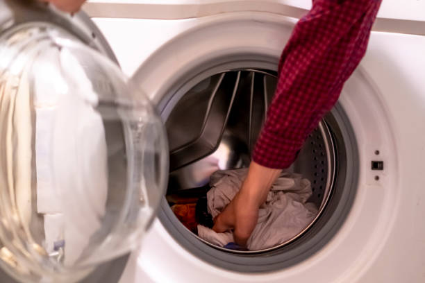 istock close up hands loading dirty clothes into washing machine at home bathroom f 1055612084