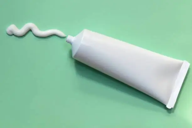 A line of compounded cream squirted out of a white, plastic ointment tube onto a green background.