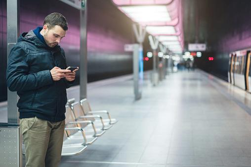 Young adult Caucasian man using his mobile phone in the metro station.