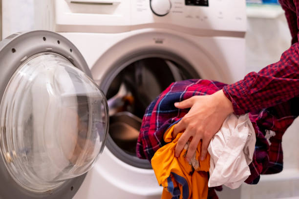 istock close up hands loading dirty clothes into washing machine at home bathroom f 1055643324