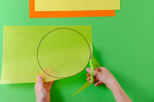 istock child's hands cut circle on transparent paper with scissors, top view, on green 1055645000