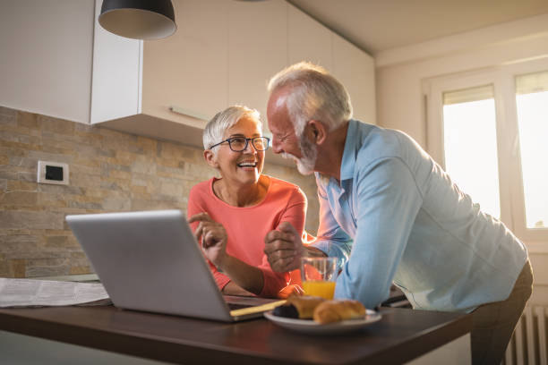 istock Modern senior couple eating breakfast in a kitchen and looking at a laptop 1055658670
