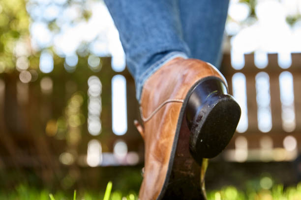 Feet of a mature woman wearing a blue jeans, red shirt and brown shoes in rear view