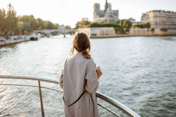 Woman enjoying landscape view on Paris city from the boat Young woman tourist enjoying beautiful landscape view on the riverside with Notre-Dame cathedral from the boat during the sunset in Paris seine river stock pictures, royalty-free photos & images