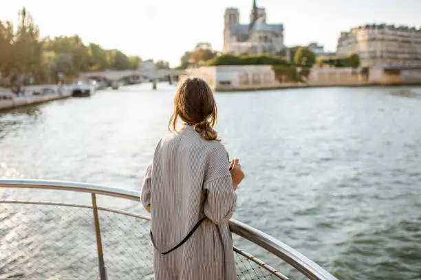 Young woman tourist enjoying beautiful landscape view on the riverside with Notre-Dame cathedral from the boat during the sunset in Paris