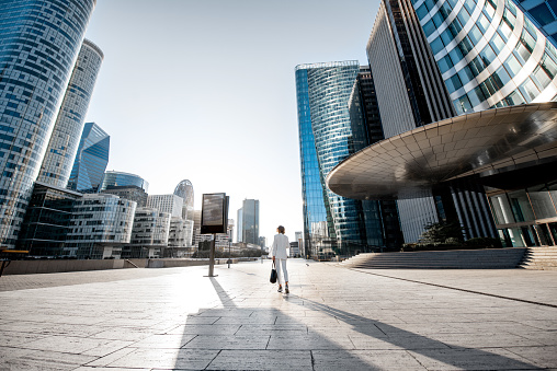 Business woman at the financial district with beautiful skyscrapers on the background during the morning light in Paris. Wide panoramic view