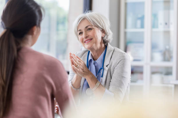 Female doctor encourages patient Caring senior doctor gestures as she talks with a female patient. womens issues photos stock pictures, royalty-free photos & images