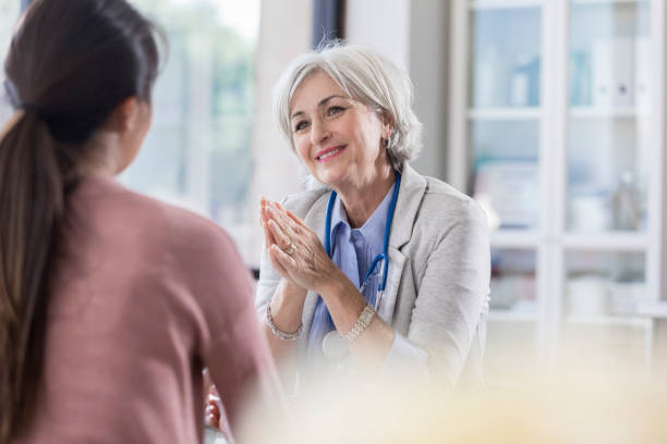Female doctor encourages patient Caring senior doctor gestures as she talks with a female patient. gray hair young woman stock pictures, royalty-free photos & images