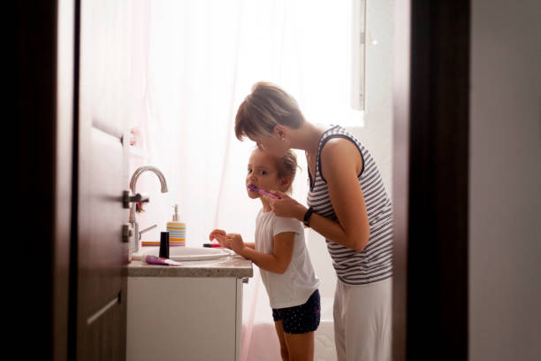 istock Mom helping young daughter brush teeth 1055691646