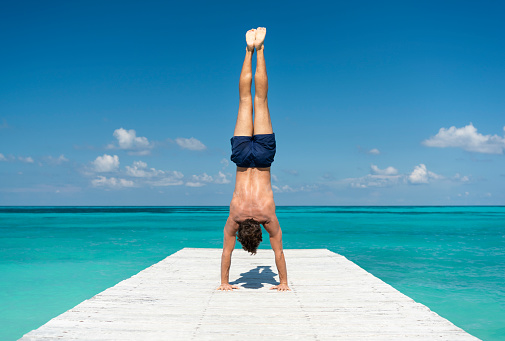 Muscular athletic man pressing a handstand on a pier in Cancun, Mexico