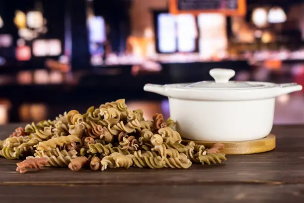 Lot of whole twisted raw pasta fusilli variety in a ceramic stewpan with restaurant in background