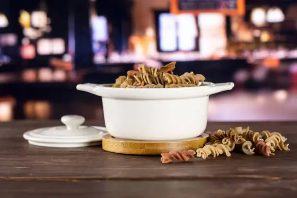 Lot of whole raw pasta fusilli variety in a ceramic stewpan with restaurant in background