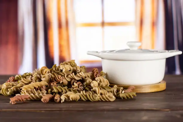 Lot of whole twisted raw pasta fusilli variety in a ceramic stewpan with silk curtains behind