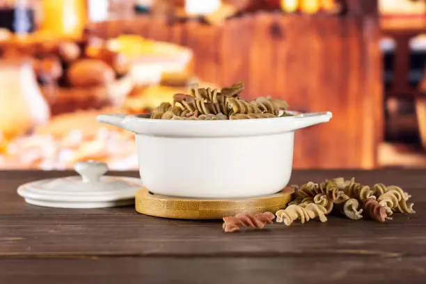 Lot of whole raw pasta fusilli variety in a ceramic stewpan with rustic wood kitchen in background