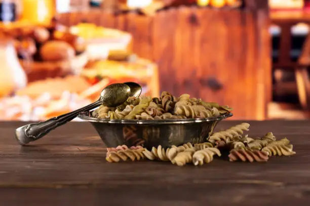 Lot of whole raw pasta fusilli variety in old iron bowl with rustic wood kitchen in background