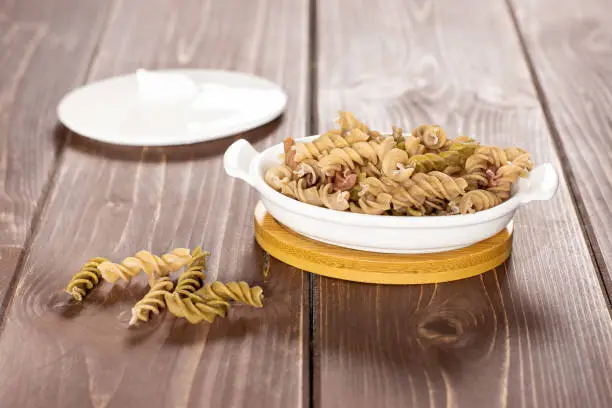 Lot of whole twisted raw pasta fusilli variety in a ceramic stewpan on brown wood