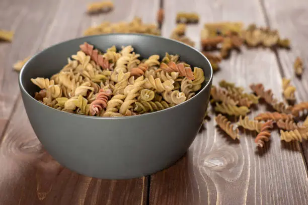 Lot of whole twisted raw pasta fusilli variety in a grey ceramic bowl on brown wood