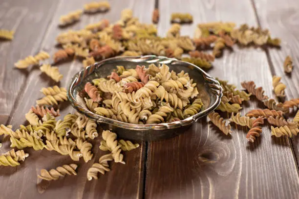Lot of whole twisted raw pasta fusilli variety in old iron bowl on brown wood