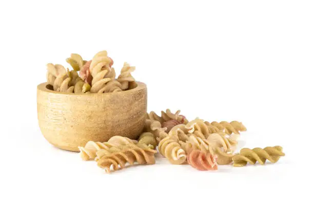 Lot of whole twisted raw pasta fusilli variety with wooden bowl isolated on white background