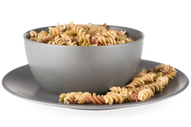 Composition lot of whole raw pasta fusilli variety in a grey ceramic bowl isolated on white background