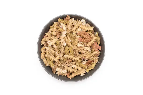 Lot of whole raw pasta fusilli variety in a grey ceramic bowl flatlay isolated on white background