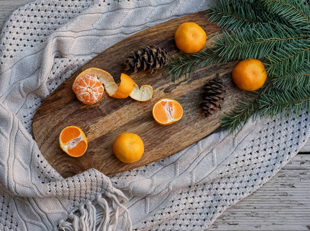 istock Tangerines fir tree brunches, pine cones on wooden kitchen board in rustic style on white wooden table background and gray knitted cloth. Christmas food decorations. Table setting. Flat lay copy space 1055707802