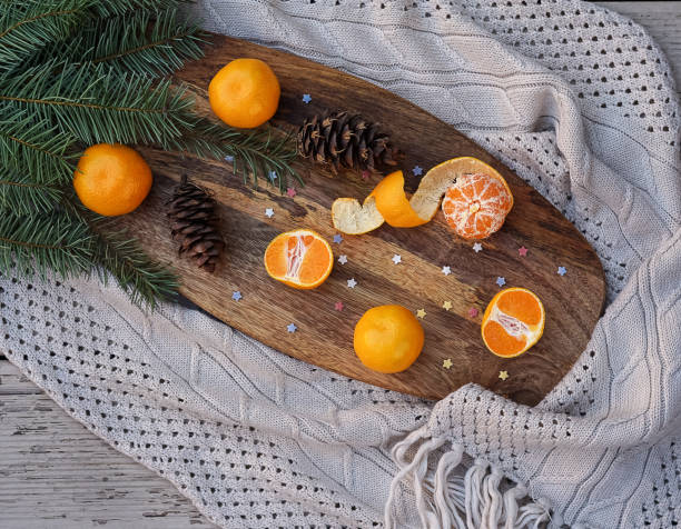 istock Tangerines fir tree brunches, pine cones on wooden kitchen board in rustic style on white wooden table background and gray knitted cloth. Christmas food decorations. Table setting. Flat lay copy space 1055707816