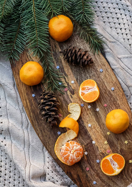 istock Tangerines fir tree brunches, pine cones on wooden kitchen board in rustic style on white wooden table background and gray knitted cloth. Christmas food decorations. Table setting. Flat lay copy space 1055707820