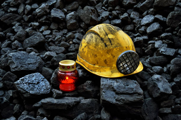 istock Lighted vigil light candle with the miner belongings (helmet, gloves, pickaxe, shovel, vest, belt) 1055709080