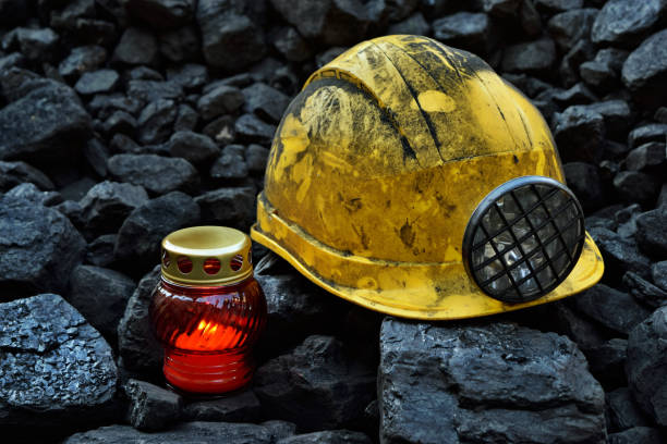 istock Lighted vigil light candle with the miner belongings (helmet, gloves, pickaxe, shovel, vest, belt) 1055709400