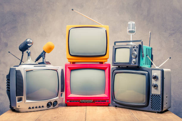 Retro old TV set receivers and microphones on table front textured concrete wall background. Broadcasting concept. Vintage style filtered photo