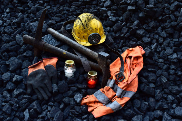 istock Lighted vigil light candle with the miner belongings (helmet, gloves, pickaxe, shovel, vest, belt) 1055709732