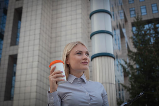 Businesswoman holding cup against buildings.