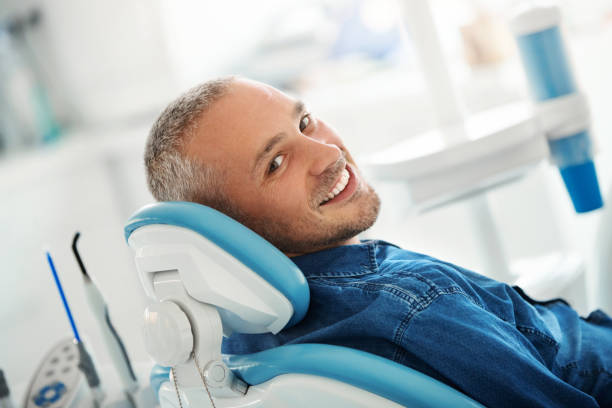 Successful dentist appointment. Closeup over the shoulder view of a cheerful early 40's male patient happily smiling to the camera after his dental procedure. dentists chair stock pictures, royalty-free photos & images