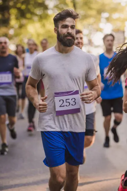 Young man feeling determined while running a marathon race through nature. Other people are in the background.