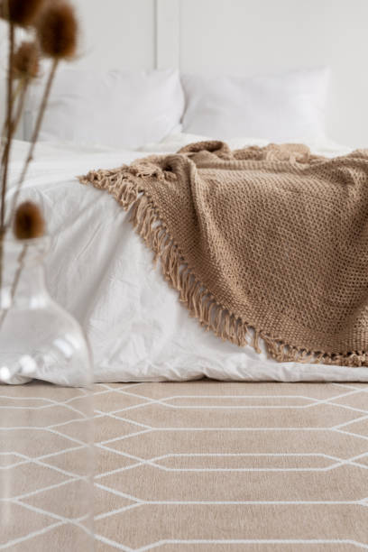 istock Patterned carpet in natural bedroom interior with brown blanket on white bed. Real photo 1055867286
