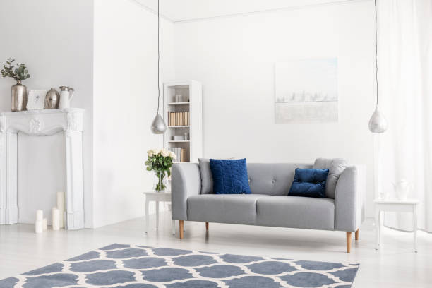 istock Patterned blue carpet in front of grey sofa in white apartment interior with flowers and lamps. Real photo 1055867332
