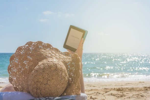 istock Woman relaxes while reading an e-book on the beach 1055867792