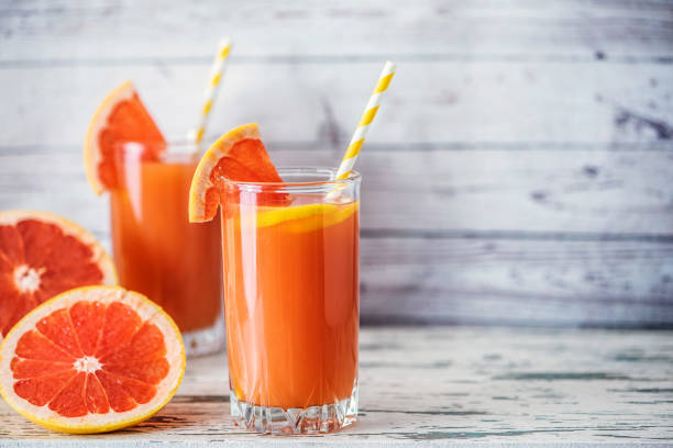 istock Fresh grapefruits and two glasses of grapefruit juice on light wooden table. With copy space 1055867836