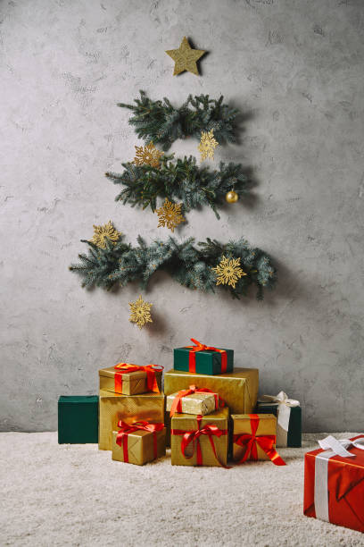 istock handcrafted Christmas tree hanging on grey wall, gift boxes on floor in room 1055868532