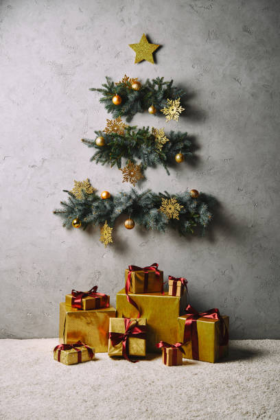 handmade Christmas tree and star hanging on grey wall, gift boxes on floor in room