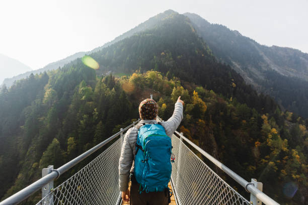 Solo hiker pointing with hand on suspension bridge Solo hiker on suspension bridge between two mountain valleys pilgrimage photos stock pictures, royalty-free photos & images