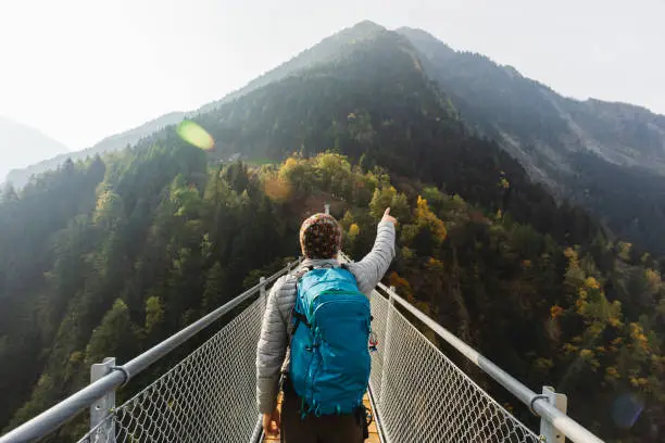 Photo of Solo hiker pointing with hand on suspension bridge