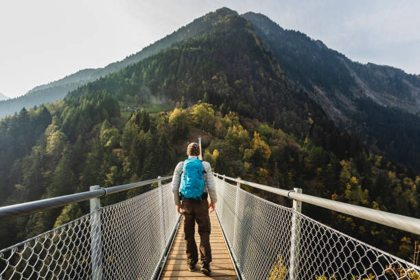 Man walking on suspension bridge between two mountain valleys