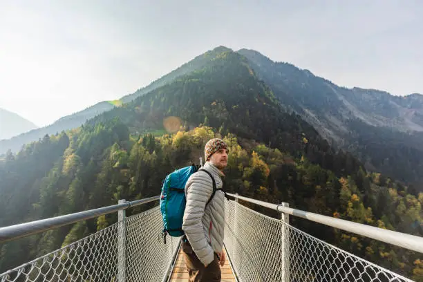 Man looking at view on suspension bridge between two mountain valleys