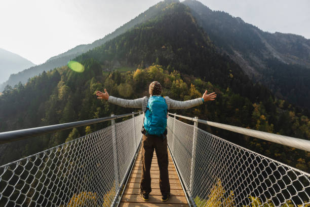 Solo hiker with open arms on suspension bridge between two mountain valleys
