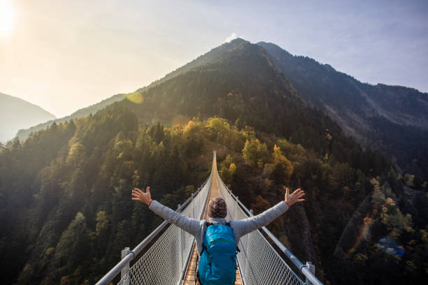 Solo hiker with open arms on suspension bridge between two mountain valleys
